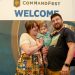 A family with a small baby posing in front of the Welcome banner